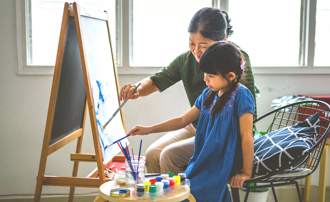  A grandparent painting on an easel with their grandchild
