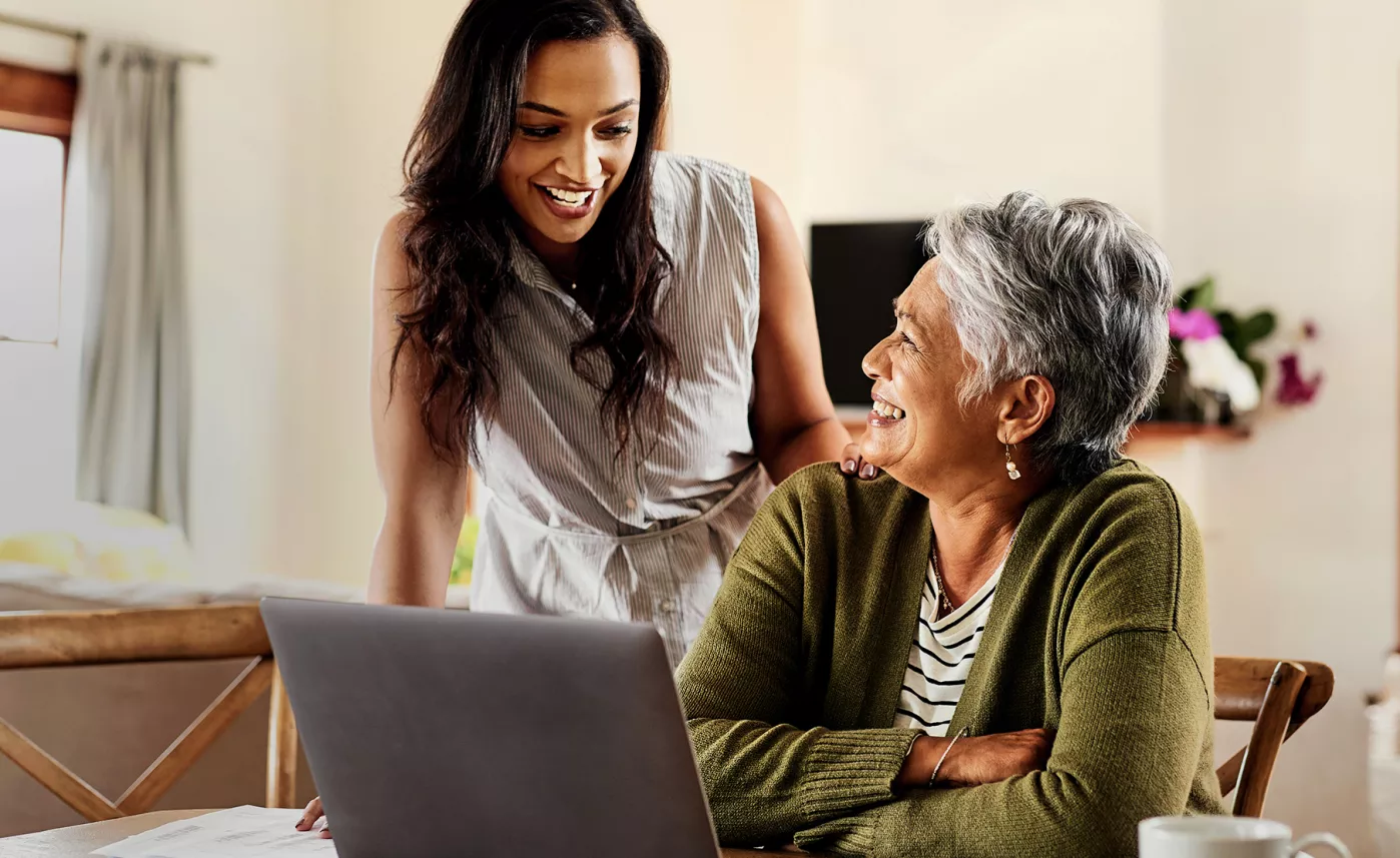  A senior woman laughs with her adult daughter as they review information on a laptop.
