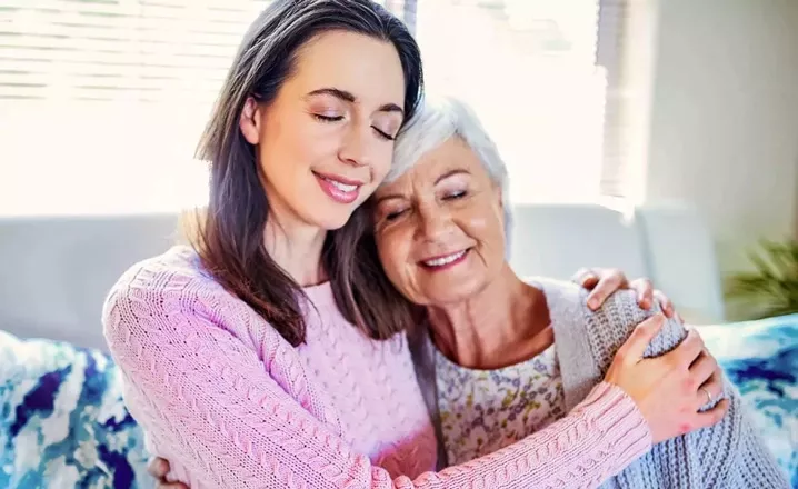  A woman smiles and hugs her elderly mother.
