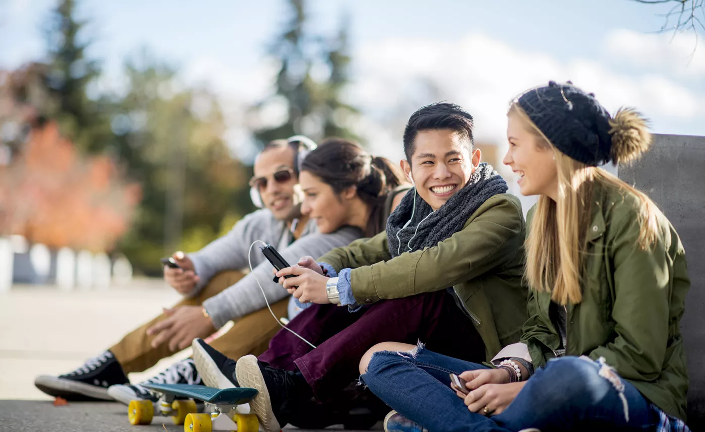  Four college students sit in a park and laugh together.
