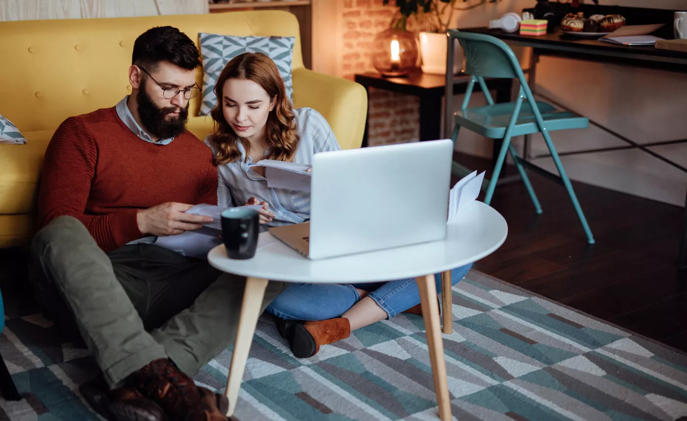  A young couple reviews their retirement account on printed documents, with a laptop open in front of them.
