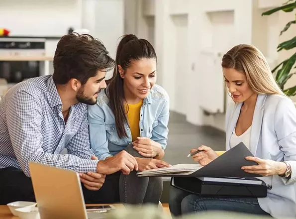  A financial advisor speaks with a young couple in her office, going over documents about beneficiaries.
