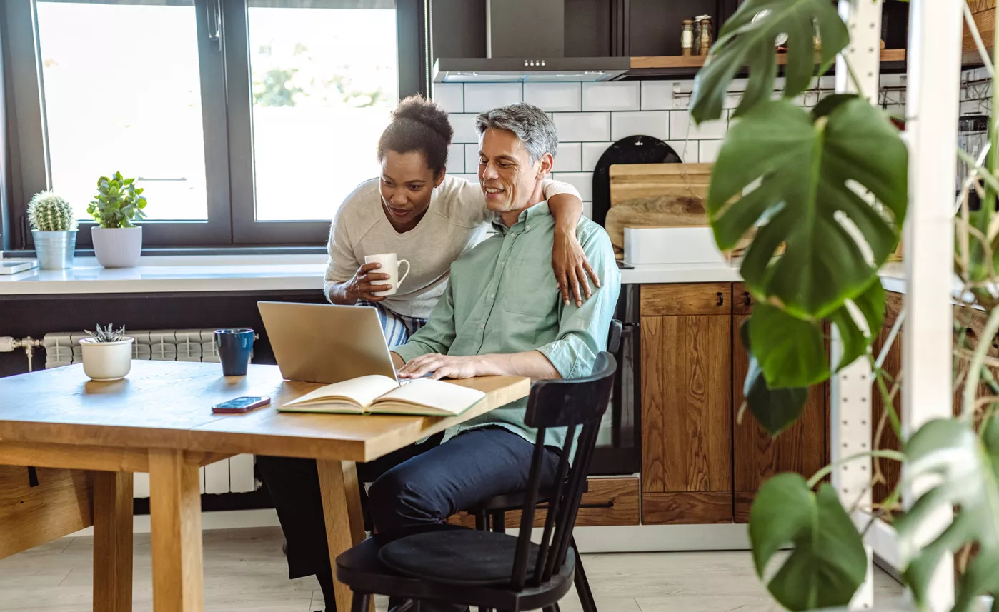  couple sitting at the kitchen table looking at a laptop
