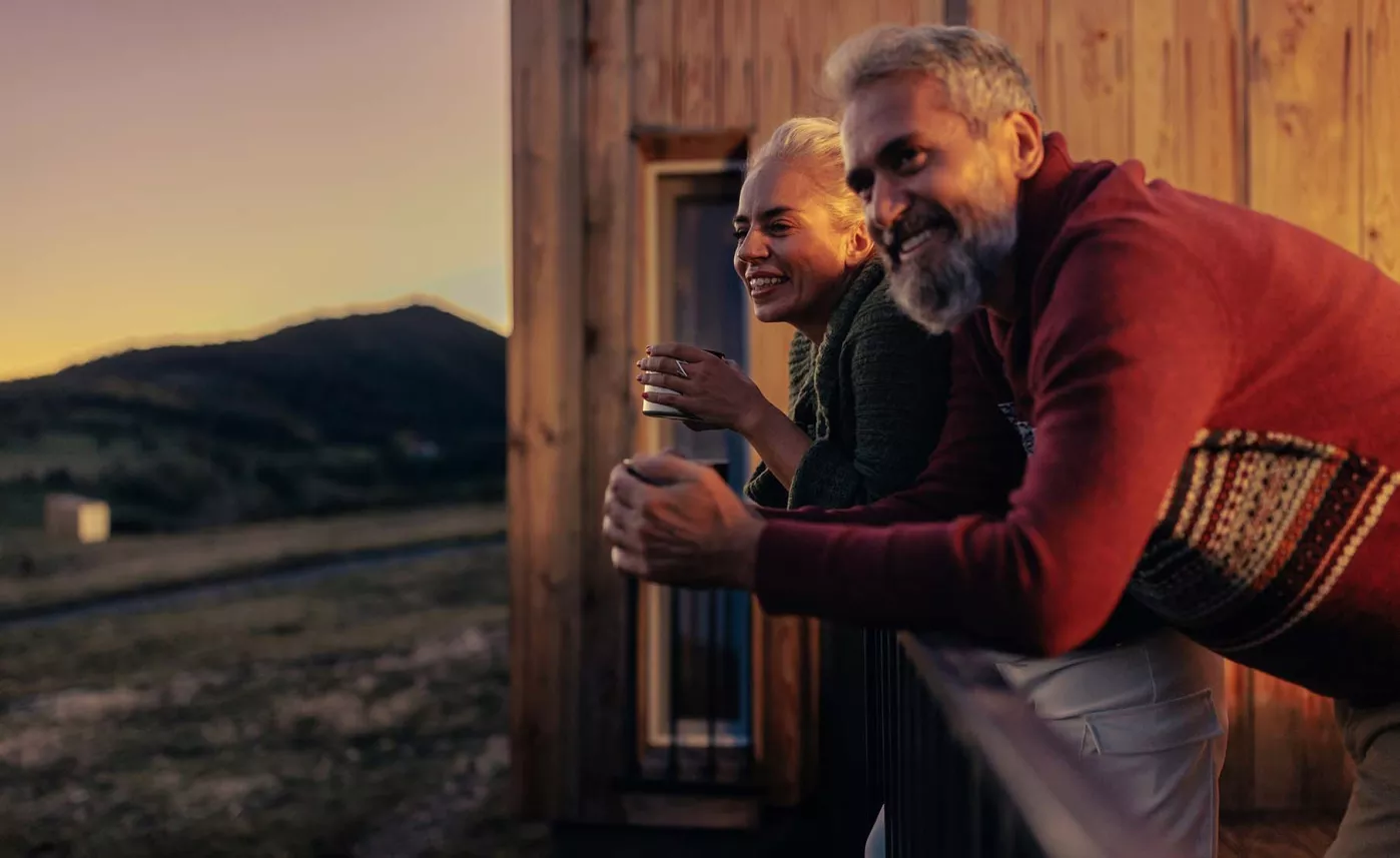  A couple standing on a balcony looking out across mountains as dusk.
