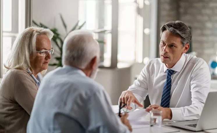 An Edward Jones advisor discusses finances with an elderly couple in his branch office.