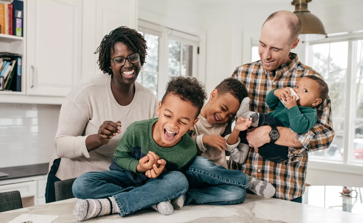  Young parents laugh with their three young boys in the kitchen.
