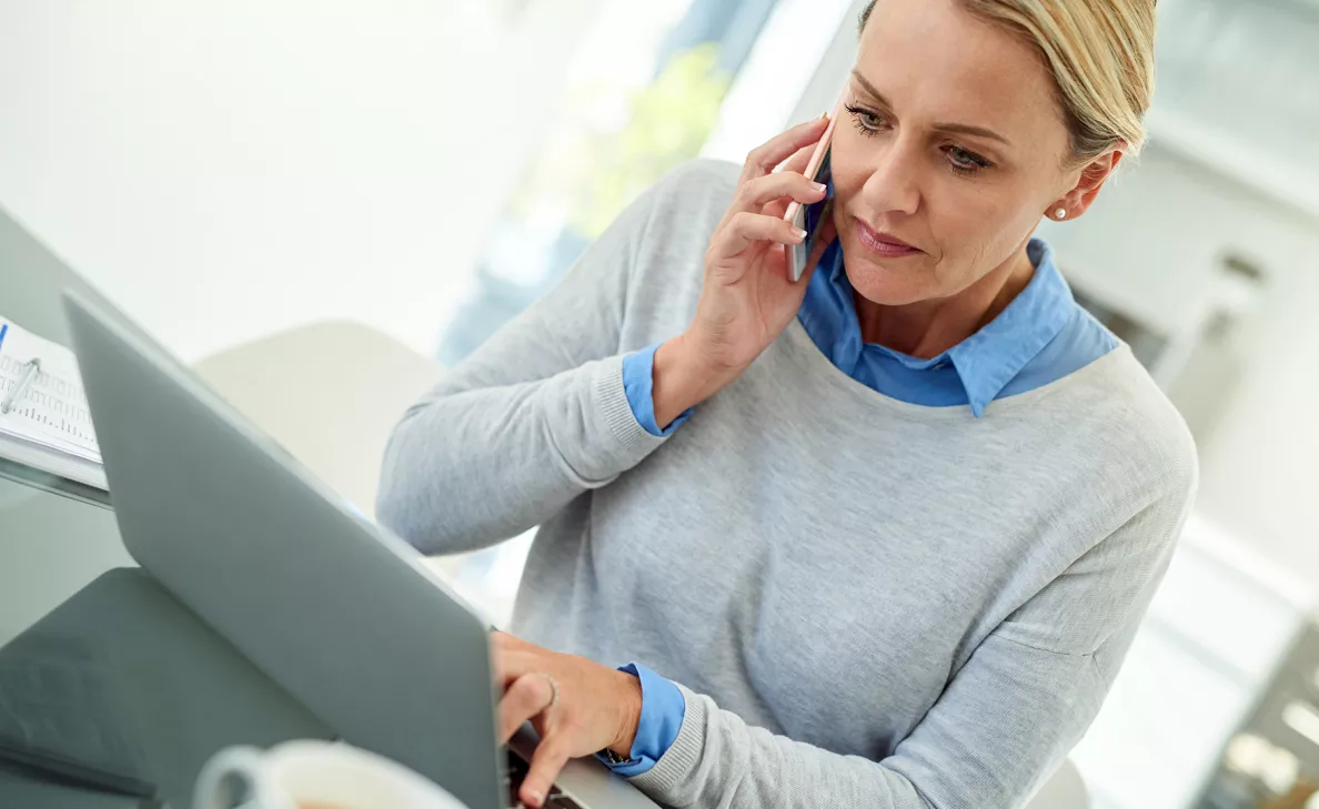  Une femme tape sur son ordinateur portable pendant un appel téléphonique.
