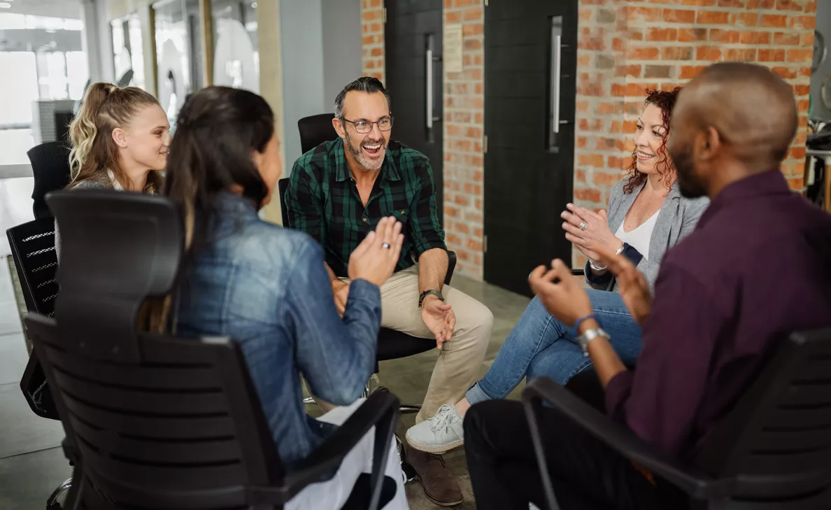  Un groupe d’adultes discutent en cercle dans un immeuble de bureaux à la mode.
