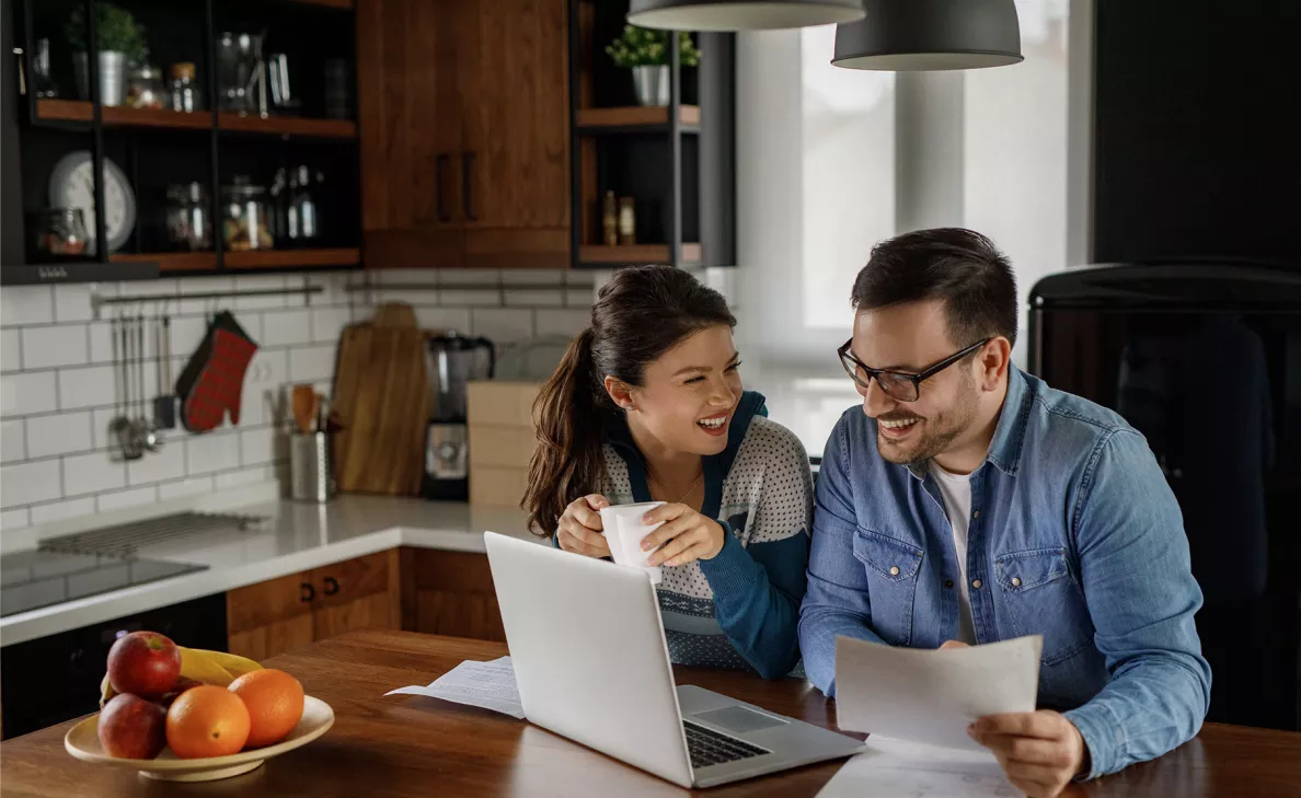  Un jeune couple examine des documents de retraite et son compte de retraite sur son ordinateur portable dans sa cuisine.
