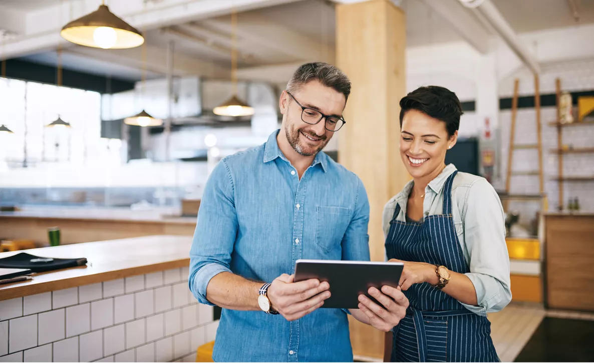  A financial advisor discusses account information on a tablet with a small business owner in her cafe.
