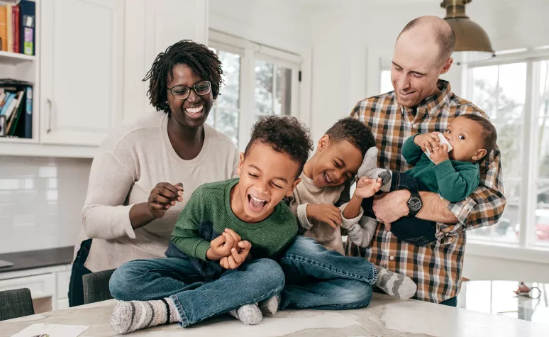 Young parents laugh with their three young boys in the kitchen.