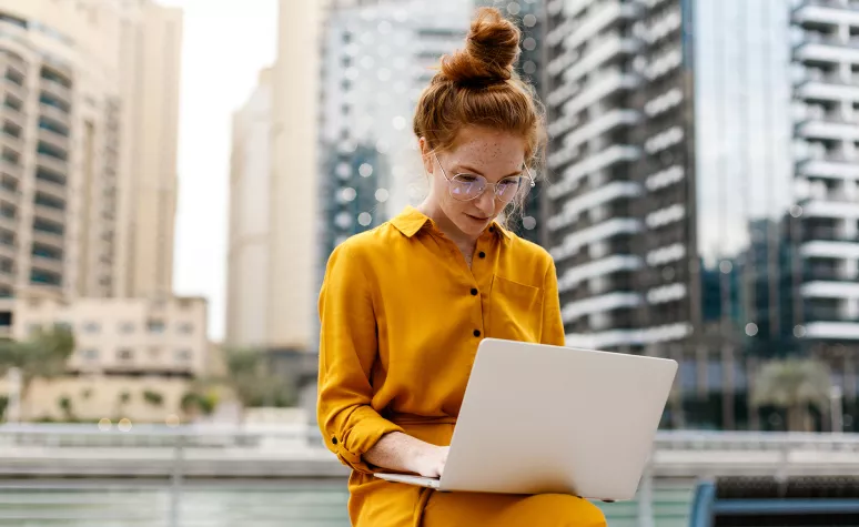 Young woman works on her laptop while sitting outside in an urban area.