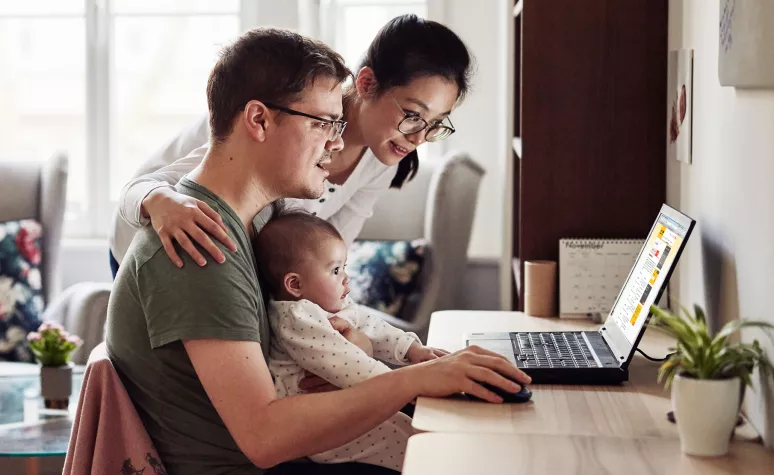 Young parents look up information on their laptop with a small infant on the father's lap.