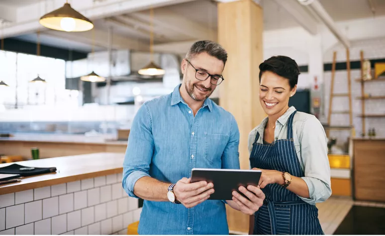 Un représentant en services financiers discute dans un café avec sa propriétaire des renseignements de compte qui sont affichés sur une tablette.