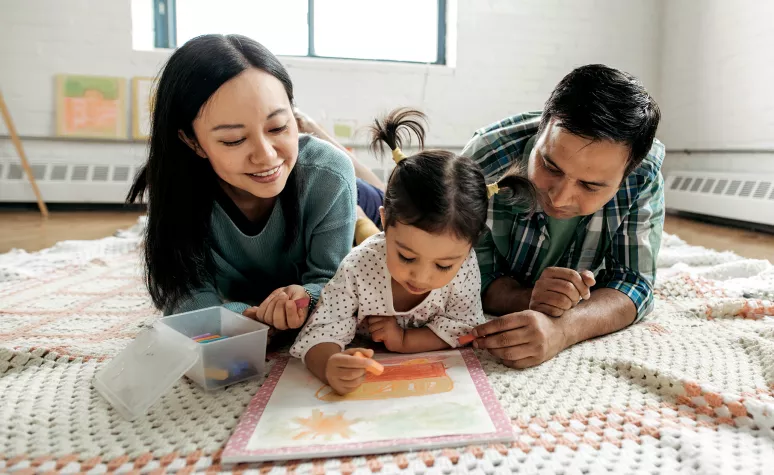 Young parents sit with their toddler daughter as she colors.