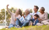 A family of three generations poses for a photo in a park on a sunny day.