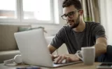 Un jeune homme travaille sur son ordinateur portable à sa table de cuisine.