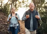 A married couple smile as they walk through a nature trail on a sunny day.