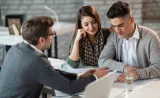 A young couple sit in an office, looking over documents with their Edward Jones financial advisor.