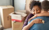 A hugging couple, surrounded by moving boxes.