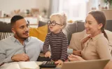 De jeunes parents assis avec leur petite fille pendant qu’elle joue avec une calculatrice.