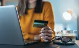 A woman reads her credit card number while typing into her laptop.