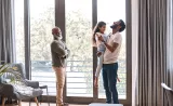 A young father hold his young daughter in a sunny living room, while a grandfather smiles at them.