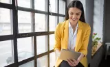 Une jeune femme souriante passe ses placements en revue assise à côté d’une grande fenêtre .