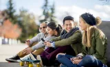 Four college students sit in a park and laugh together.