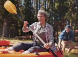 A retirement-aged woman kayaks in a lake with her husband on a sunny day.