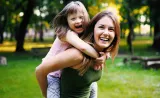 Une jeune mère tient son enfant dans ses bras; ils sourient dans le parc par une journée ensoleillée.