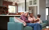 Two grandparents sit with their infant son in their home.