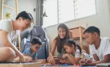 Parents playing a board game on the floor with three young kids.